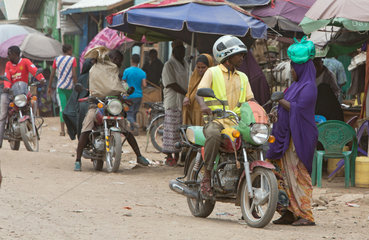 Kakuma  Kenia - Strassenszene mit Menschen und Motorraedern. Motorradverkehr auf einer belebten unbefestigten Strasse.