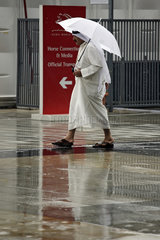 Dubai  Mann in arabischer Tracht laeuft bei Regen unter seinem Regenschirm