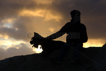 Wustrow  Deutschland - Silhouette  Junge sitzt am Abend mit seinem Hund auf einer Duene