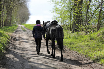 Melbeck  Reiterin fuehrt ihr Pferd einen Sandweg entlang