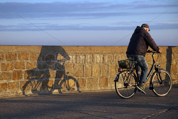 Warnemuende  Radfahrer wirft einen Schatten an eine Mauer