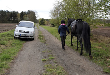 Melbeck  Reiterin fuehrt ihr Pferd an einem parkenden Auto vorbei