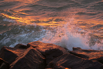 Warnemuende  Wellen brechen sich im Abendlicht an Felsgestein