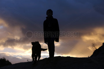Wustrow  Deutschland - Silhouette  Junge steht am Abend mit seinem Hund auf einer Duene