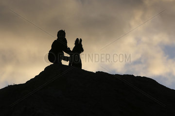 Wustrow  Deutschland - Silhouette  Junge hockt am Abend mit seinem Hund auf einer Duene