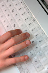 Eine Kinderhand schreibt auf einer Computertastatur.