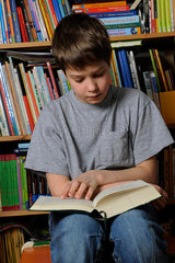 Junge liest Buch vor Buecherregal