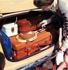 Frau verstaut Urlaubsgepaeck im Kofferraum  1958