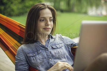 Woman reclining in hammock with laptop computer