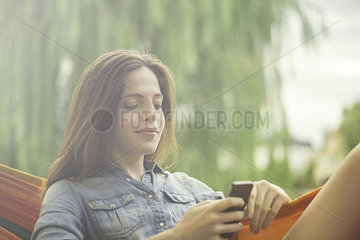 Woman reclining in hammock with smartphone
