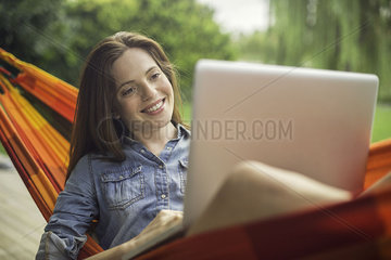 Woman reclining in hammock with laptop computer