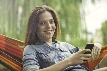 Woman reclining in hammock with smartphone
