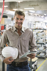 Factory worker holding hard hat and digital tablet  portrait