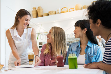 Waitress serving drinks to women in cafe