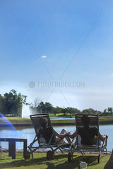 Couple relaxing in deckchairs at edge of lake