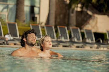 Couple soaking in pool with eyes closed