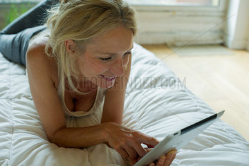 Mature woman relaxing on bed with digital tablet