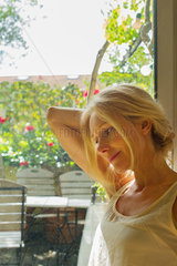 Mature woman stretching and looking away in thought beside window