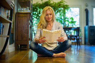 Mature woman sitting on floor at home  reading book