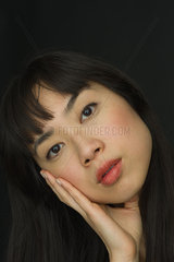 Young woman with head tilted  cheek resting on hand  portrait