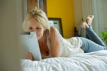 Mature woman lying on bed watching digital tablet