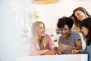 Group of young women looking at smartphone and laughing together in cafe