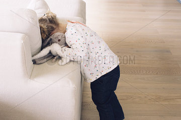 Little girl hiding her face in sofa cushions
