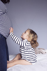 Little girl touching mother's pregnant stomach  cropped