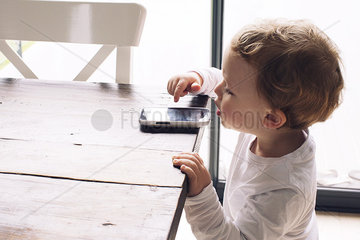 Little boy playing with smartphone left on edge of table