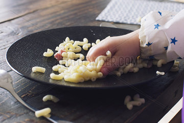 Child eating macaroni with her hand  cropped