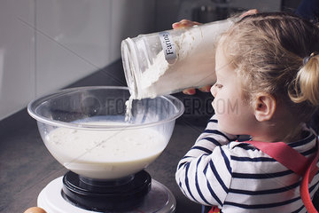 Little girl pouring flour into mixing bowl