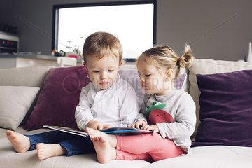 Young siblings looking at book together on sofa