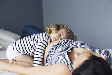 Little girl and pregnant mother lying together on bed