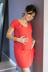 Pregnant woman leaning against wall  smiling  portrait
