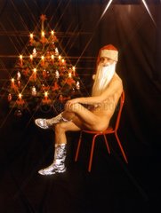 Nackter Weihnachtsmann sitzt neben Weihnachtsbaum