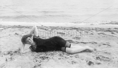 Frau posiert am Strand liegend  1920
