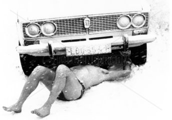 Mann liegt nackt unter Auto im Schnee