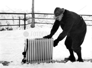 alter Mann schiebt Heizkoerper durch Schnee