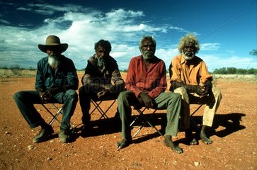 Gruppe Aborigines auf Stuehlen in der Wueste