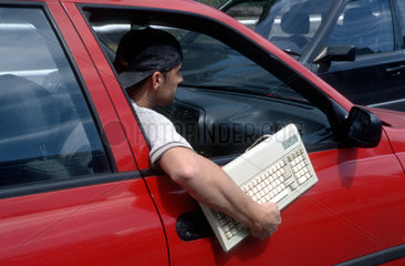 Mann haelt Tastatur aus dem Autofenster
