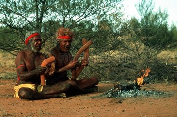 Aborigines mit Bumerang sitzen am Feuer