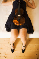 Frau liegt auf dem Bett mit Violine im Schoss