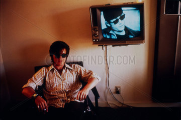 Man sitting beside a wall-mounted television screen  United States  1971.