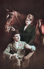 Frau und Mann in Reitdress posieren mit Pferd
