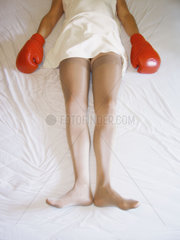 Frau liegt mit Boxhandschuhen im Bett