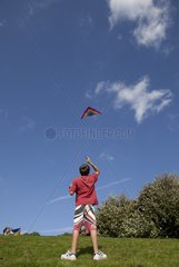 Young boy flying red kite in blue sky Broadway Tower UK