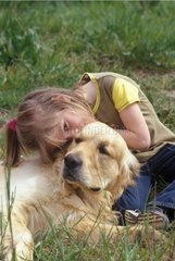 Mädchen kuschelt einen goldenen Retriever im Gras Frankreich