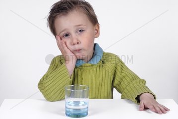 Boy dubious sitting over a glass of water