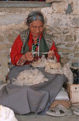 Tibetische Frau  die Wolle für einen Teppich vorbereitet