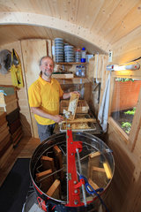 Urban Beekeeping - Ralf Schneider Rathmann  50 years old  plumber by profession  in his honey extraction cabin where the machines are powered by solar energy. Behind an extractor  he is holding a honey frame in his hands. Germany